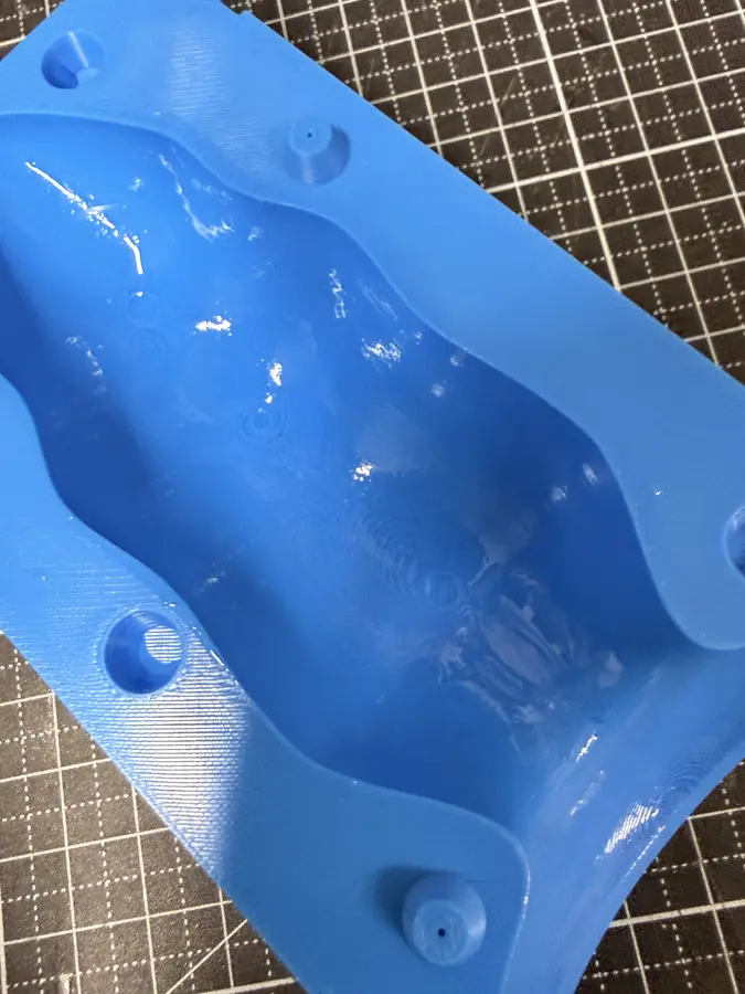 A mould half with a glossy coat of resin over the hollow.