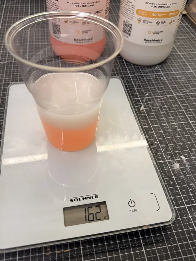 A cup on a kitchen scale reading 162 g, with part A and part B layered in it.