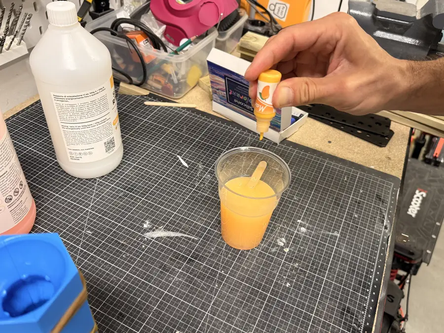 A hand drips yellow colour into a cup of mixed silicone.