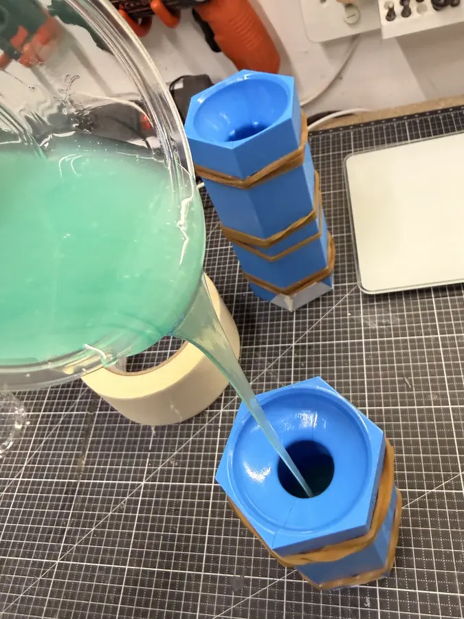 Green silicone pours from a cup into the funnel of a closed mould.
