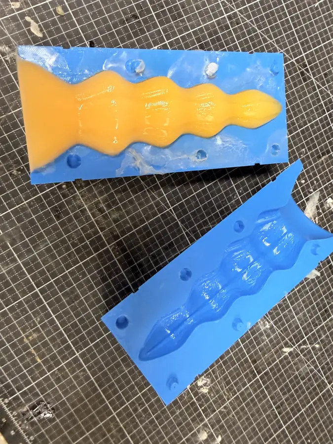 An opened mould: the yellow cast still lies in one half, the other half beside it.